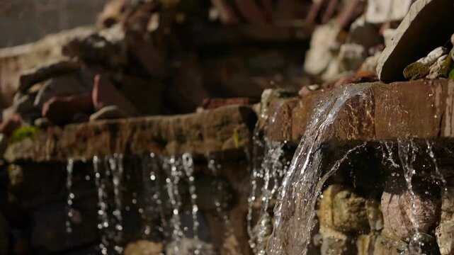 Clear water flows over a rustic stone ledge in a peaceful garden water feature at sunset