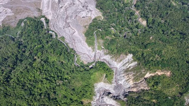 Aerial drone view of a completely dry volcanic lava channel winding through the rugged landscape of Lumajang, showcasing hardened gray sediment and deep erosion trails.