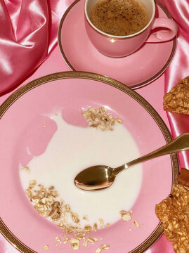 Breakfast scene with pink plate, spoon, granola, milk, and coffee cup on satin fabric