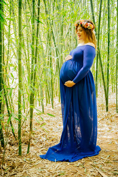 Pregnant white woman in a blue dress standing in bamboo forest
