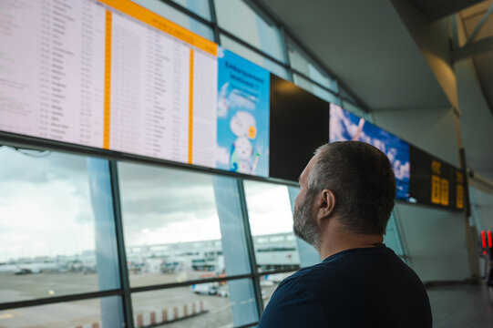 A man reads the same terminal departures board from a slight side angle near the window. A natural continuation of the moment spent checking his flight.