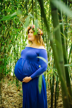 Pregnant white woman in blue dress with flower crown in bamboo forest