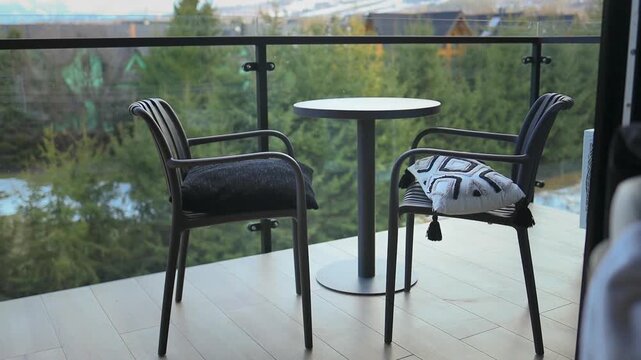 Outdoor patio view of a modern hotel or chalet balcony featuring two stylish wicker armchairs, a small round table, and a scenic green landscape in the background.