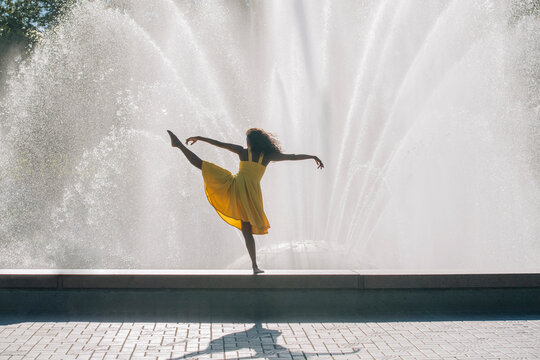 South Asian dancer performing pose in yellow dress by water fountain
