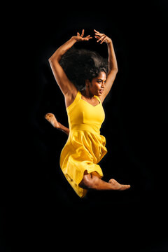South Asian woman jumping in yellow dress against dark background