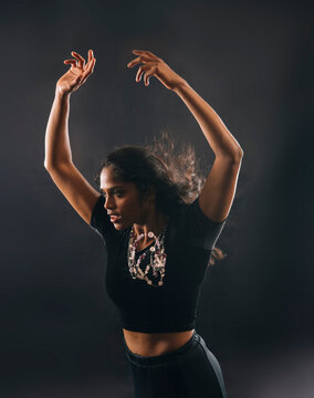 South Asian woman dancing with raised arms and black crop top