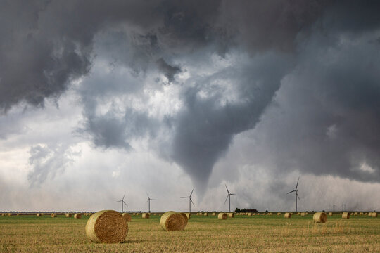 Tornado touching down in a field with hay bales and wind turbines