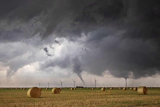 Tornado funnel cloud forming over rural field with wind turbines