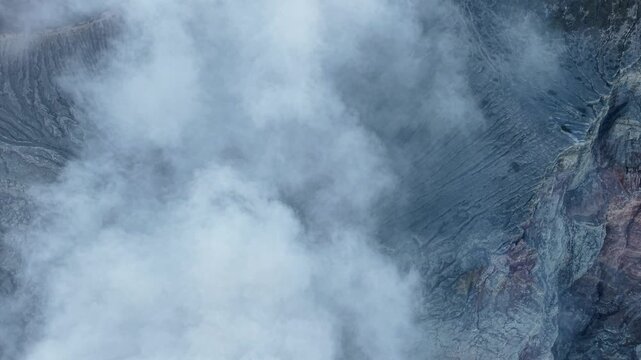Drone aerial view of smoky Mount Ijen crater with drifting steam and jagged volcanic rock