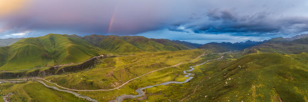 Rainbow over green hills and winding river at sunset in Kham Tibet
