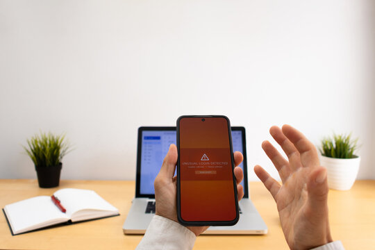 Hand holding smartphone with unusual login warning beside blurred laptop