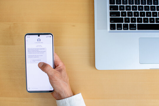 Smartphone phishing message with suspicious download link clicked on wooden desk
