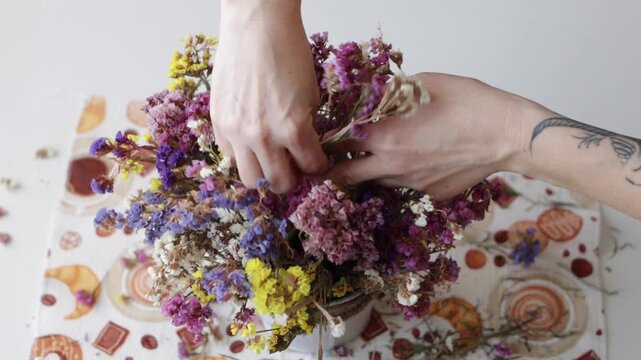 Close up top view of female hands carefully arranging colorful dried statice flowers in bucket pot