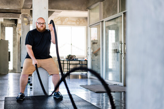Man exercises with battle ropes in a modern gym, creating powerful rope waves during an intense workout session.