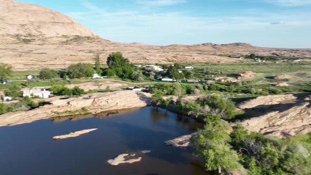 Drone video panning side to side over a lake with rocky mountains, lush greenery, and clear sky in natural daylight.