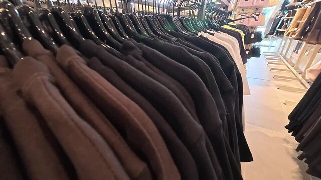 Clothing racks display neatly arranged jackets in bright retail store. Dark and brown outerwear hangs in rows, offering clear view of organized apparel inventory and shopping merchandise.