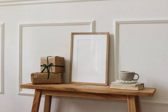 Neutral Christmas interior still life. Vertical wooden picture frame mockup, poster template. Wrapped gifts, Coffee Tea cup on old wooden console table. Festive Winter holidays home decor, birthday.