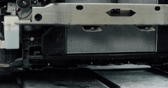 Mechanic cleaning EV radiator and condenser by spraying water and blowing air dry in service garage