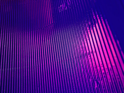 Neon purple-pink light background. Corrugated texture. Fluorescent pink purple color gradient glow reflection on parallel lines pattern dark black abstract overlay. Horizontal grooved metal surface.