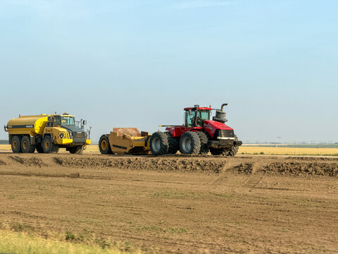 Saskachewan, Canada - August 20, 2026: Case IH Steiger tractor pulling land scraper beside Komatsu water truck during field leveling on Saskatchewan prairie farmland