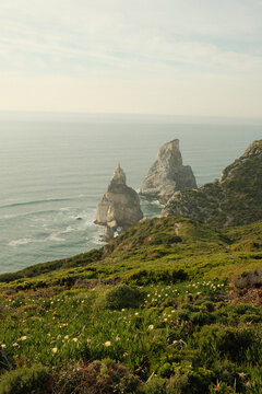 Famous Praia da Ursa sea stacks and green coastal cliffs with wildflowers above Atlantic ocean, Sintra, Portugal