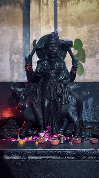A dark stone statue of Shani Dev displayed in a devotional setting, surrounded by traditional offerings and subtle warm illumination.