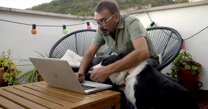Man and Dog on Balcony Working Remotely: A man with glasses and a beard, accompanied by his loyal border collie, works diligently on his laptop on a cozy balcony.