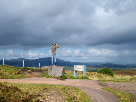 Visitor on a rock in Glendoebeg overlooking the landscape near Loch Ness and Fort Augustus, Scottish Highlands
