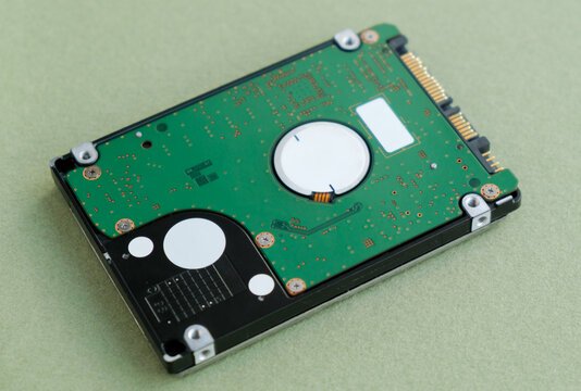 Technology and hardware photography featuring a disassembled internal hard disk drive (HDD) circuit board on a textured green background, representing computer components.