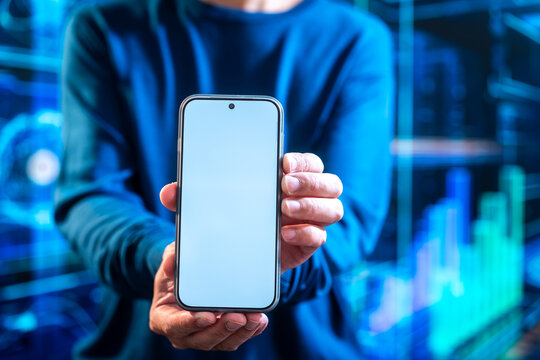 Person holding a smart phone with a blank screen in front of glowing financial charts, ideal for mobile banking, trading, fin tech, and digital technology concepts.
