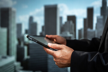 Close-up of a business professional using a mobile device near a window, with a softly blurred modern city skyline and skyscrapers in the background. © M+Isolation+Photo