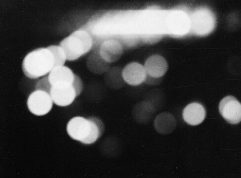Retro film overlay with scratches, dust, grain, light leaks and bokeh on a black background, creating a distressed monochrome cinematic effect for posters and design.