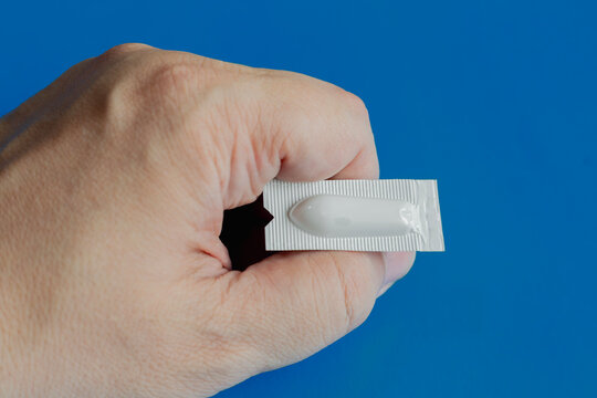 Hand Holding Suppository Blister Pack Medicine for Rectal Treatment and Symptom Relief on Blue Background