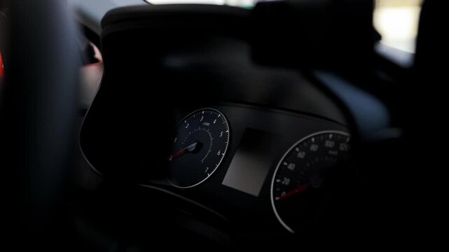 Close up view of a modern automobile instrument panel with illuminated dials and digital display in the dark. Vehicle interior details with speedometer, tachometer, and cockpit elements. Performance