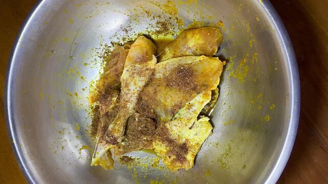 Top view close up footage of Indonesian Ayam Bumbu Kuning, chicken pieces marinated with yellow turmeric spices simmering in a large metal cooking pan, traditional Asian food cooking process