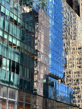 Exterior view of adjoining glass curtain walls on a business office building in an urban setting, where reflections of surrounding buildings create a distorted, rippled pattern across the facade. 