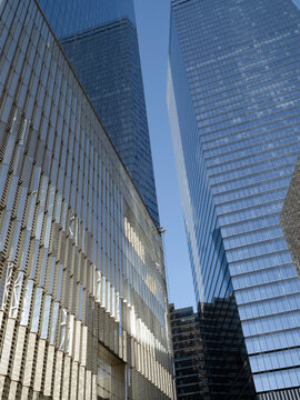 Low-angle view of glass-clad business office towers in Lower Manhattan, separated by a narrow gap of blue sky. 