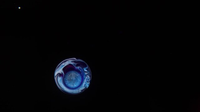 Against a black background, an abstract sphere with shimmers of blue, white, and purple colors hovers, with a shimmering core in the center &mdash; a mesmerizing cosmic object in the shape of a drop.