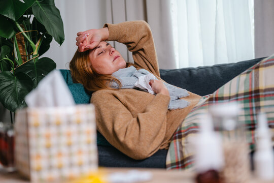 Woman resting on a sofa with a tissue and blanket while feeling unwell.Cold and flu, fever, fatigue, seasonal illness and recovery.