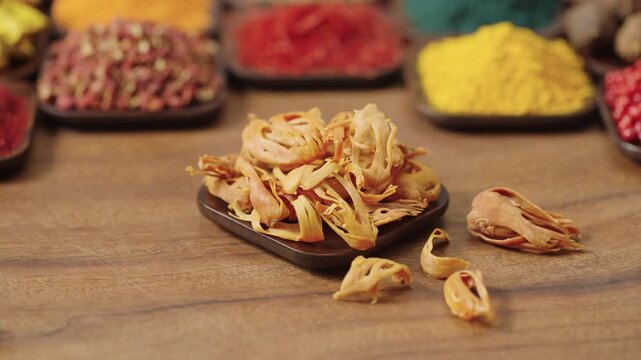 mace nutmeg shell in a square bowl on a wooden table, surrounded by various spices and herbs.