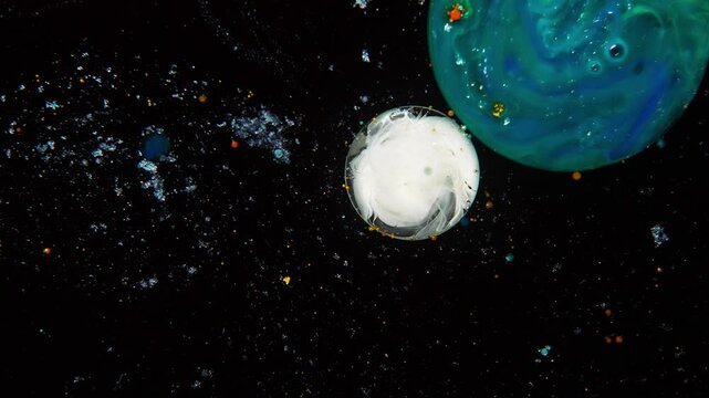 Two abstract droplets, resembling the Earth and the Moon, connect in the black space.
