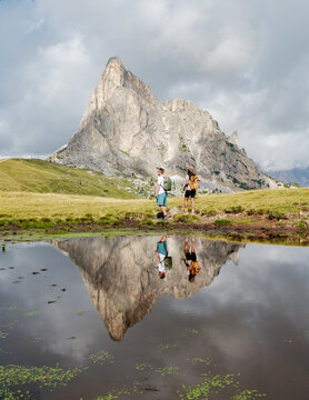 In the stunning Dolomites of Italy, two hikers stroll along a serene landscape, their reflections glimmering on a calm pond.