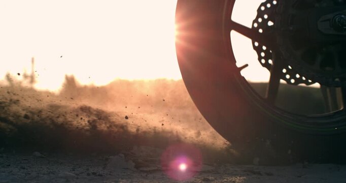 Racing motorcycle skidding on a dusty dirt road at 1000 fps, throwing gravel and dust into the air with a dramatic lens flare. Cinematic slow motion evoking speed, power and adrenaline.