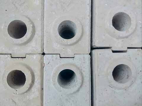 Close-up of stacked white concrete blocks with circular hollow openings, showing geometric repetition, rough construction textures, masonry materials, and structural design.