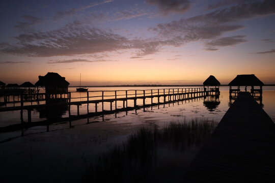 Silhouetted wooden pier with palapas over a lagoon at sunrise, Mexico