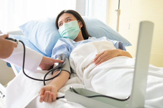 Hospital patient wearing a face mask while a medical professional measures blood pressure, highlighting routine care, recovery and compassionate healthcare in a bright clinical room for medi