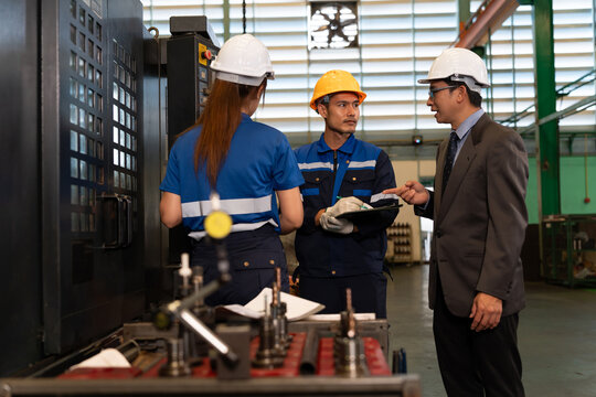 Industrial workers discuss factory operations beside machinery and equipment, representing teamwork, manufacturing, engineering, workplace safety, productivity, and management.