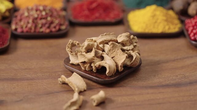 lodhra bark from the plant symplocos racemosa in a square bowl on a wooden table, surrounded by various spices and herbs.
