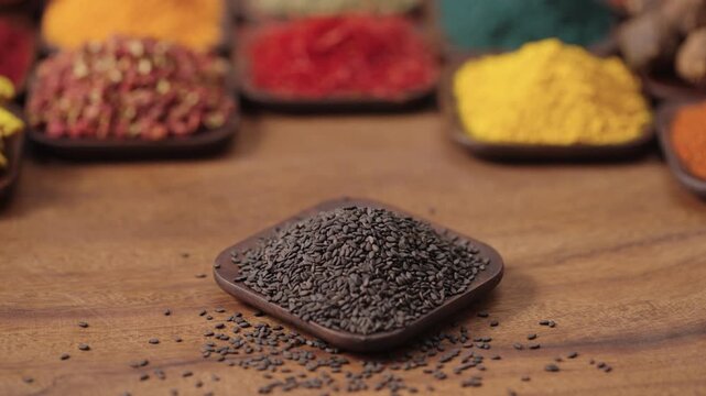 black sesame seeds, oilseed plant sesamum indicum in a square bowl on a wooden table, surrounded by various spices and herbs.