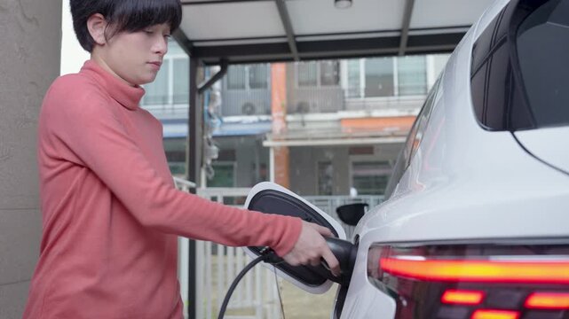 Woman unplugs the charging cable of an electric vehicle (EV car), Sustainable clean energy
